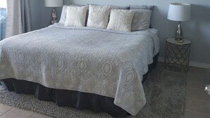 Een slaapkamer met een bed, twee bedlampjes, een plafondventilator, een raam met gordijnen en een kunstwerk aan de muur.