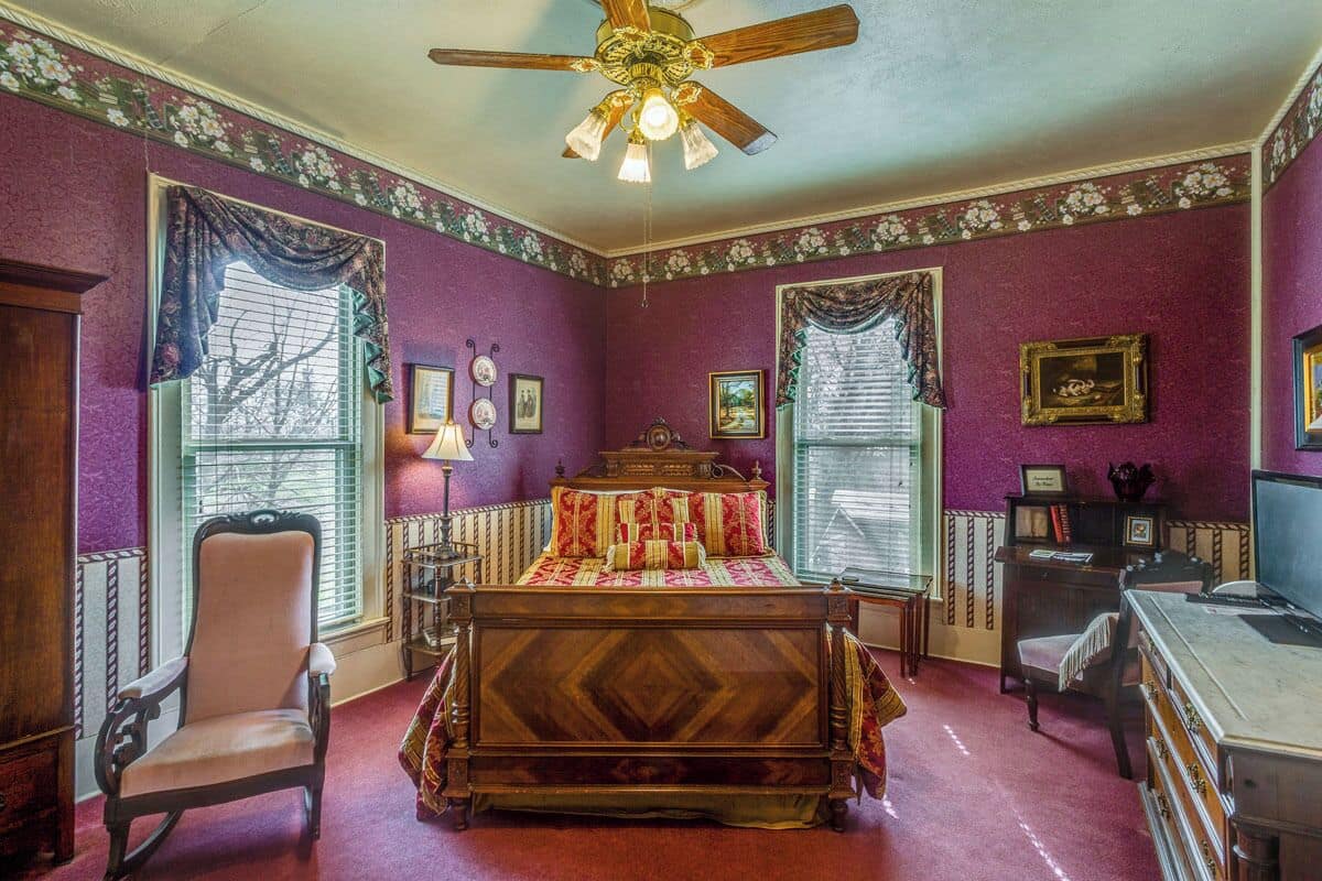 A bedroom with a wooden bed, a chair, a desk, and a ceiling fan.