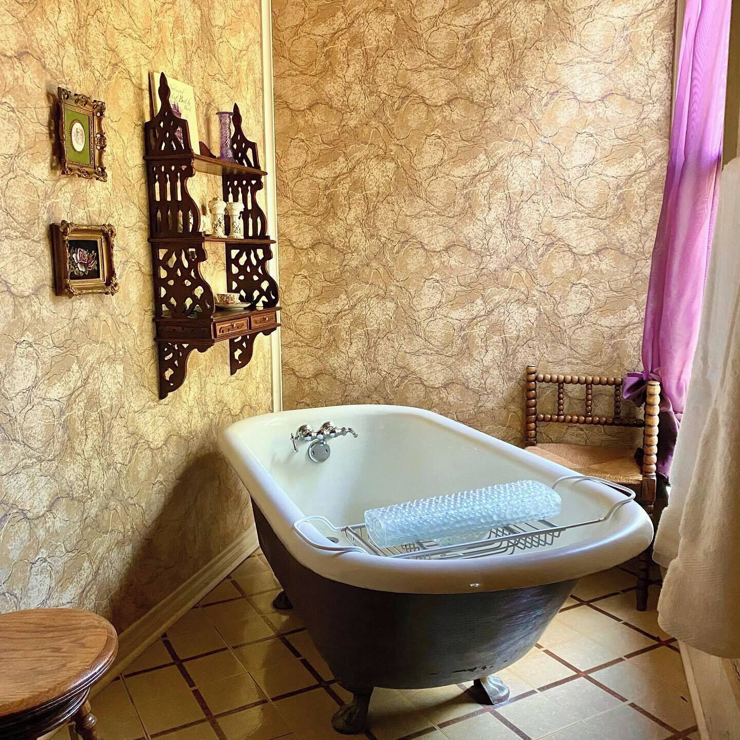 A bathroom with a clawfoot bathtub, wooden wall decor, and a tiled floor.