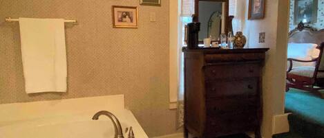 A bathroom with a bathtub, a wooden dresser, and framed pictures on the wall.