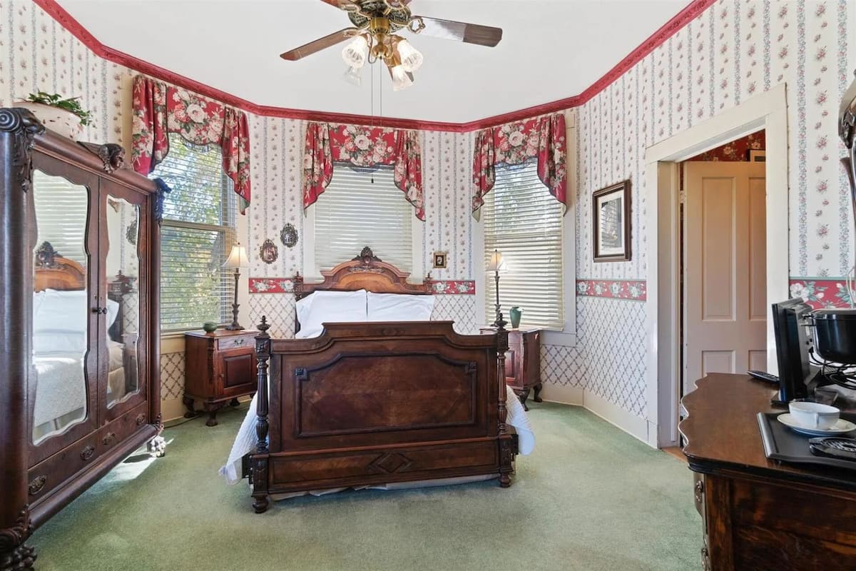 A bedroom with a wooden bed, a ceiling fan, and floral wallpaper.
