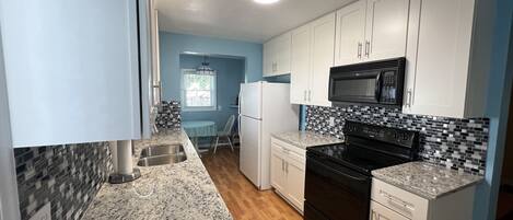 Una cocina compacta con alacenas blancas, una estufa negra y un salpicadero de azulejos.