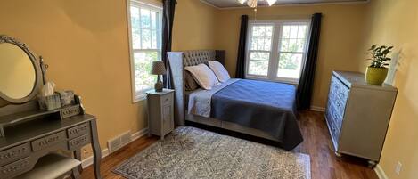 A bedroom with a bed, dresser, vanity, and a ceiling fan.