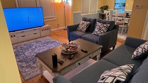 Un salon avec un téléviseur, des canapés, une table basse et, au fond, un coin repas.