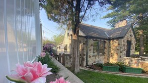 Un bâtiment en pierre doté d’une cheminée en pierre, d’une fenêtre et d’un petit jardin agrémenté de jardinières vertes.