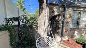 Une chaise suspendue blanche dans un jardin, avec un mur en pierre et une fenêtre.