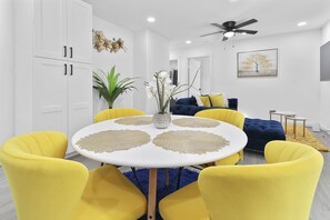 Enjoy meals in this stylish dining area with a round table and six chairs, surrounded by a blue sofa and artwork.