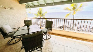 Ein Balkon mit Tisch und Stühlen, mit Blick auf einen Strand mit Palmen und das Meer.