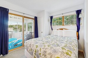 A bedroom with a bed, a window with curtains, a sliding glass door to a balcony with outdoor furniture.