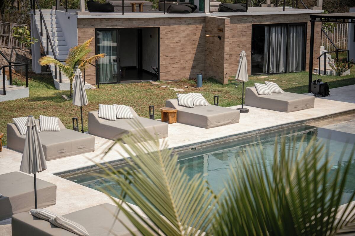 A modern outdoor pool area with multiple lounge chairs and a staircase leading to an upper level.