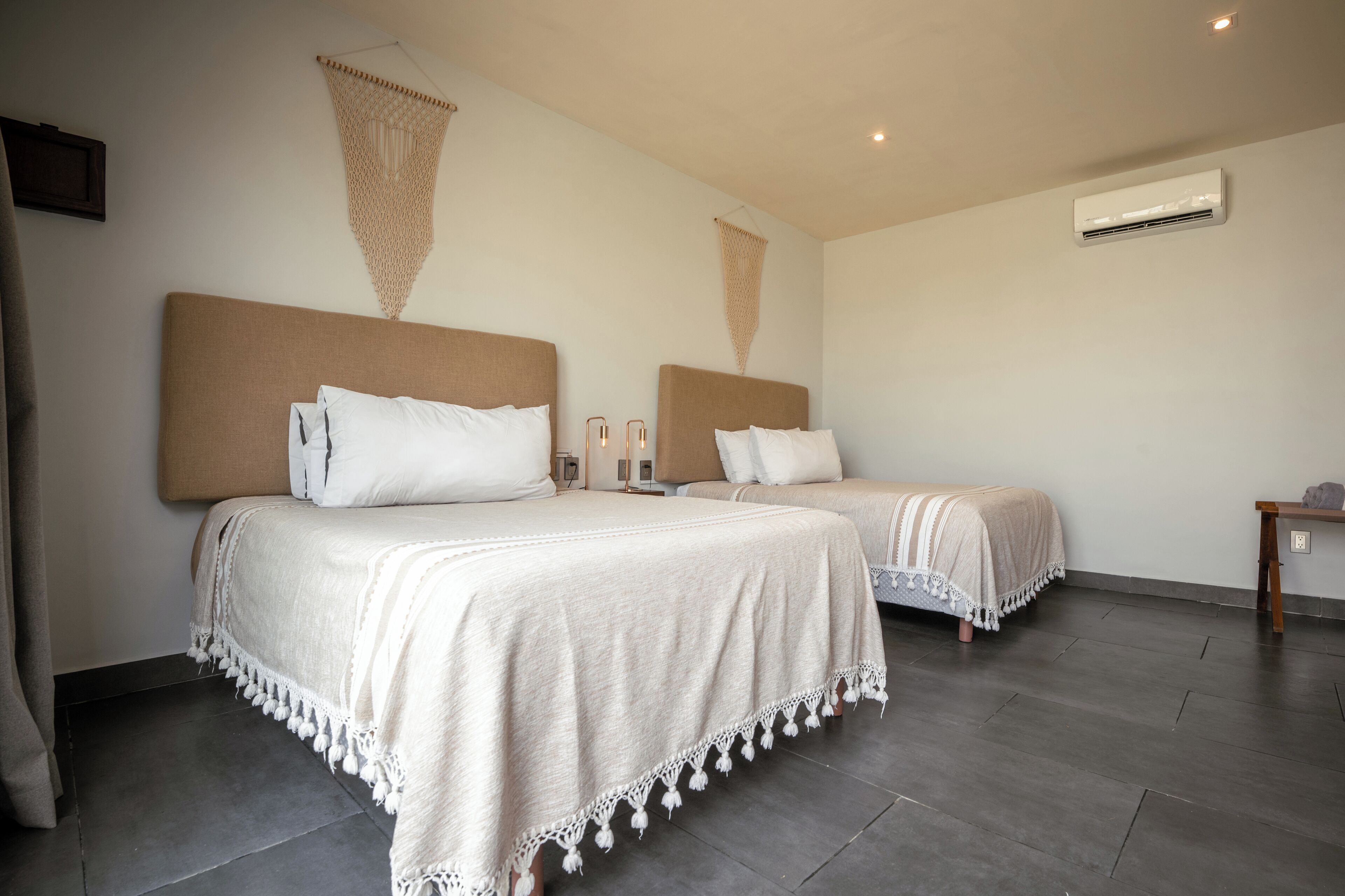 Ein Hotelzimmer mit zwei Betten, jeweils mit Kopfteil, Nachttisch und einer wandmontierten Klimaanlage.
