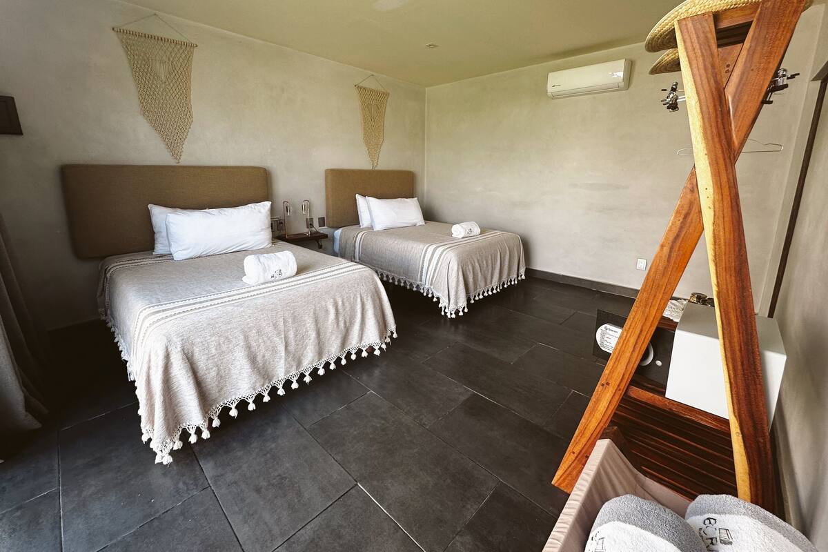 A hotel room with two beds, a wooden headboard, a small table, and a hanging basket.