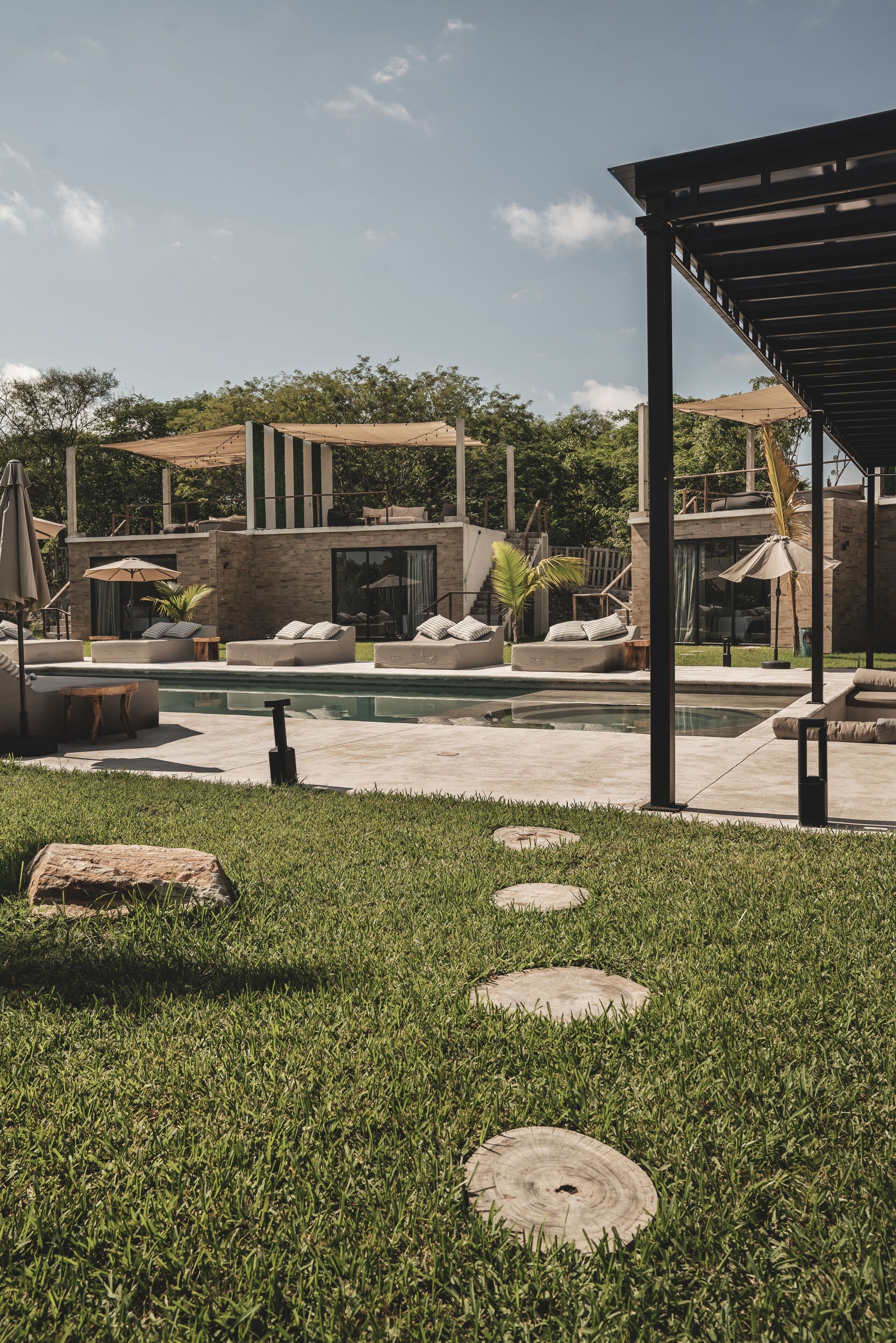 Un área de piscina moderna al aire libre con sillones de descanso y una zona de estar cubierta.