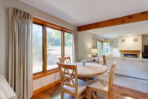 Relax in a spacious living area with a fireplace, sofa, and dining table, surrounded by large windows offering a view of the outdoors.