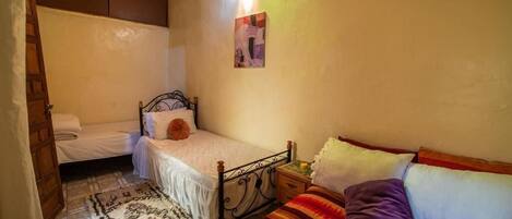 A small, cozy bedroom with a single bed, a nightstand, a bedside table, and a wall-mounted light fixture.