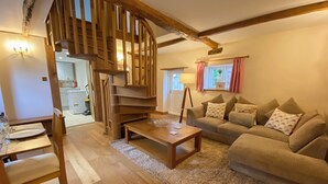 A cozy living room with a wooden staircase, a sofa set, a dining table, and a kitchen in the background. - 2 bedroom accommodation in Hothfield (Hothfield)