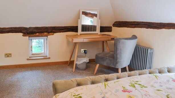 A bedroom with a sloped ceiling, a wooden desk, a chair, a radiator, a window, and a bed with a floral bedspread. - 2 bedroom accommodation in Hothfield (Hothfield)