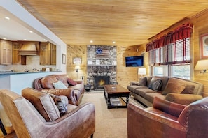 A cozy living room with leather sofas, a stone fireplace, and wooden cabinetry. - Captivating lakefront home with private dock, row boat, firepit, and lake views (Meredith)