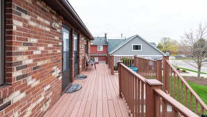 A wooden deck with a brick wall, a red door, and a gray house in the background.