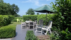 Une terrasse extérieure avec une table et des chaises, entourée de verdure et sous un ciel dégagé.