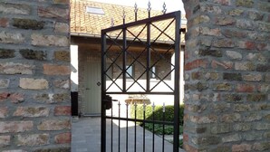 Une entrée fermée par un portail, donnant accès à un bâtiment doté d’un toit en tuiles et d’une porte.