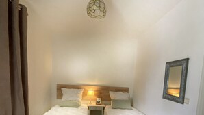 Une chambre d’hôtel avec deux lits simples, une table de chevet avec une lampe, un miroir au mur et un luminaire au plafond.