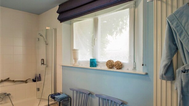 Une salle de bain avec une baignoire, une douche, une fenêtre agrémentée d’objets décoratifs et un porte-serviettes.