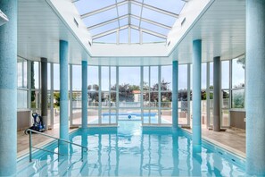 An indoor swimming pool with clear glass ceilings, large windows, and a view of the outside.