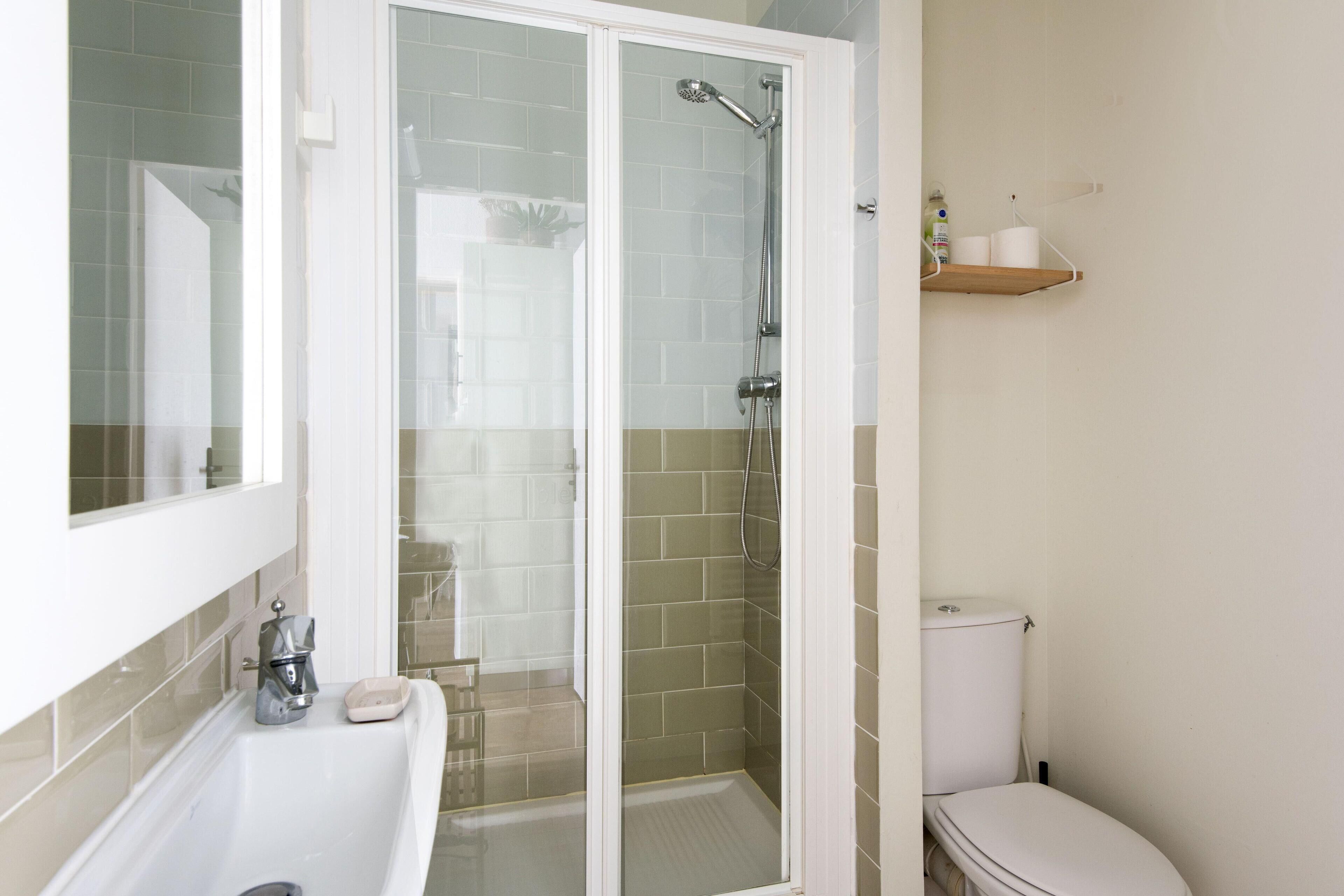 A bathroom with a glass-enclosed shower, a white toilet, and a shelf with toiletries.