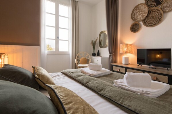 A hotel room with a bed, a desk with a television, a lamp, and a window with curtains.