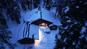 A cabin with a snow-covered roof, surrounded by trees. - Cozy Tahoe Donner Retreat – Hot Tub, Fireplace & Near Ski Resorts! (Truckee)