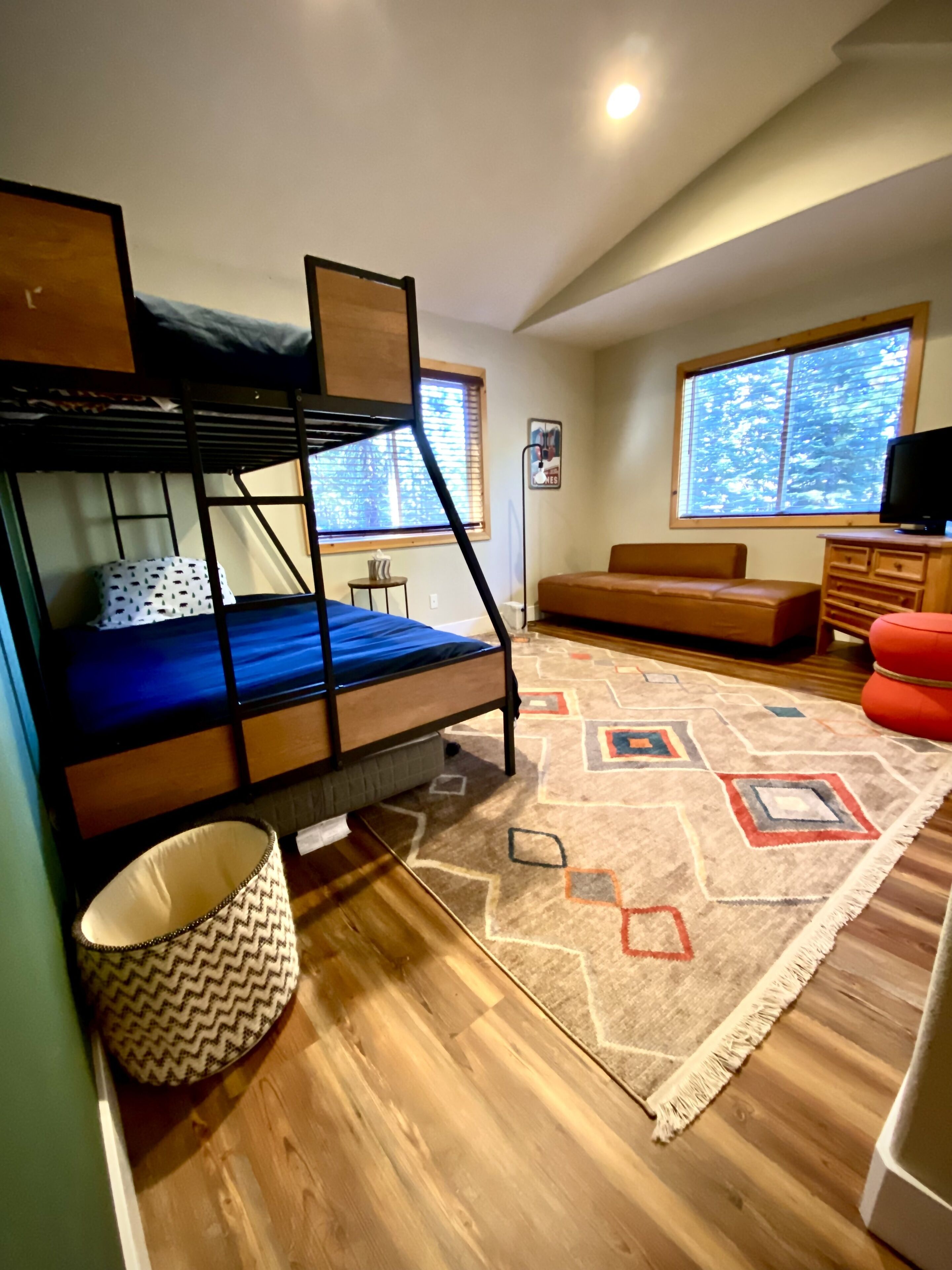 A room with a bunk bed, a sofa, a television, and a patterned rug.
