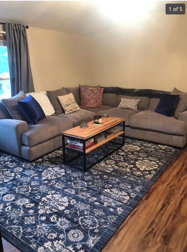 Ein Wohnzimmer mit grauem Sofa, einem Holztisch und einem gemusterten Teppich.