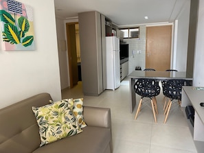 Un salon avec un canapé et une table basse, une cuisine avec un réfrigérateur et un coin repas avec des chaises.