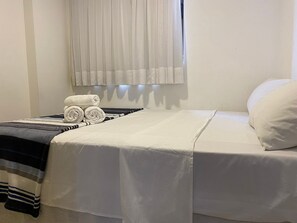 Un lit bien fait, avec des draps blancs, une couverture à rayures et des serviettes enroulées posées sur le côté.
