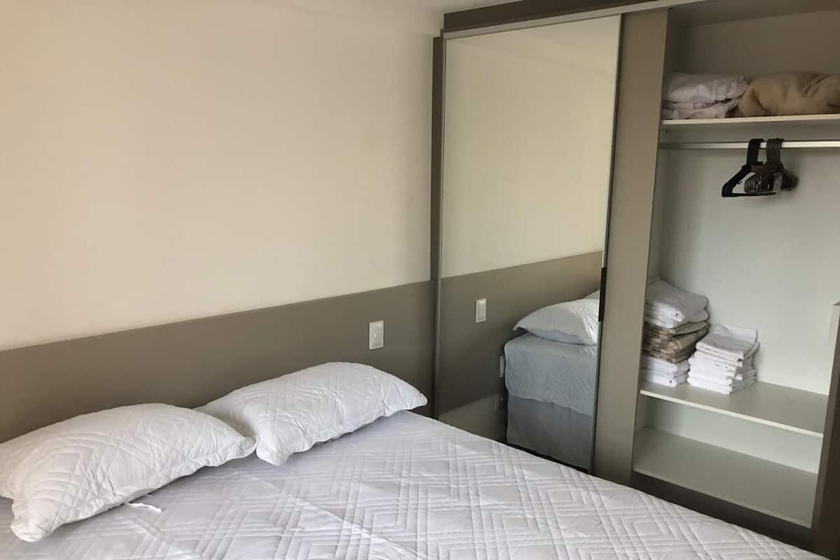 A hotel room with a bed, a wardrobe, and a shelf with folded towels.