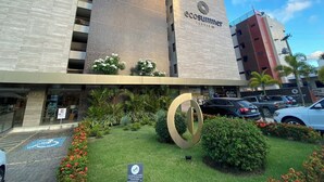 A modern building with a prominent 'ecosummit' sign, a landscaped garden with a large circular sculpture, and a parking area with cars. - Bela Hospedagem-EcoSummer Duplex Tambaú (João Pessoa)
