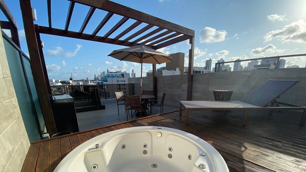 A rooftop terrace with a hot tub, outdoor furniture, and a view of the city skyline. - Bela Hospedagem-EcoSummer Duplex Tambaú (João Pessoa)