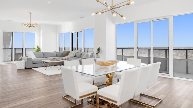 A spacious living area with a glass-top dining table, white sofas, and a large window overlooking a cityscape.
