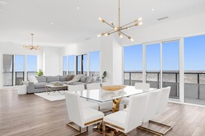 A spacious living area with a glass-top dining table, white sofas, and a large window overlooking a cityscape. - Luxury Penthouse Suite (Toronto)