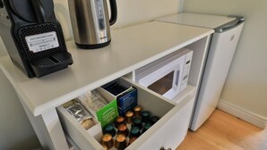 Ett litet kök med en kaffebryggare, en vattenkokare, en mikrovågsugn och en låda med te- och kaffekapslar.