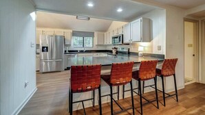 A modern kitchen with a central island, stainless steel appliances, and red woven chairs. - Secluded Retreat w Hot Tub, FirePit & Pool Access (Hedgesville)