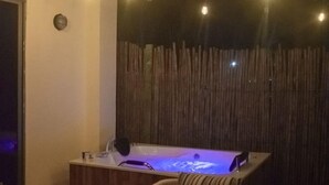 A cozy indoor setting with a wooden table and chairs, a hot tub, and string lights.