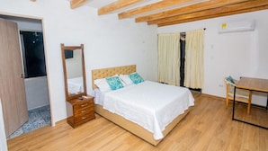 A bedroom with a wooden ceiling, a bed with white bedding, a wooden dresser, and a small table.
