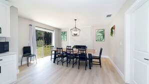 A modern kitchen with white cabinets, a dining area with a wooden table and black chairs, and a large window with a view of greenery. - ☆New☆6min to 3 Sisters Springs☆Spacious, Fun with Game room (Crystal River)
