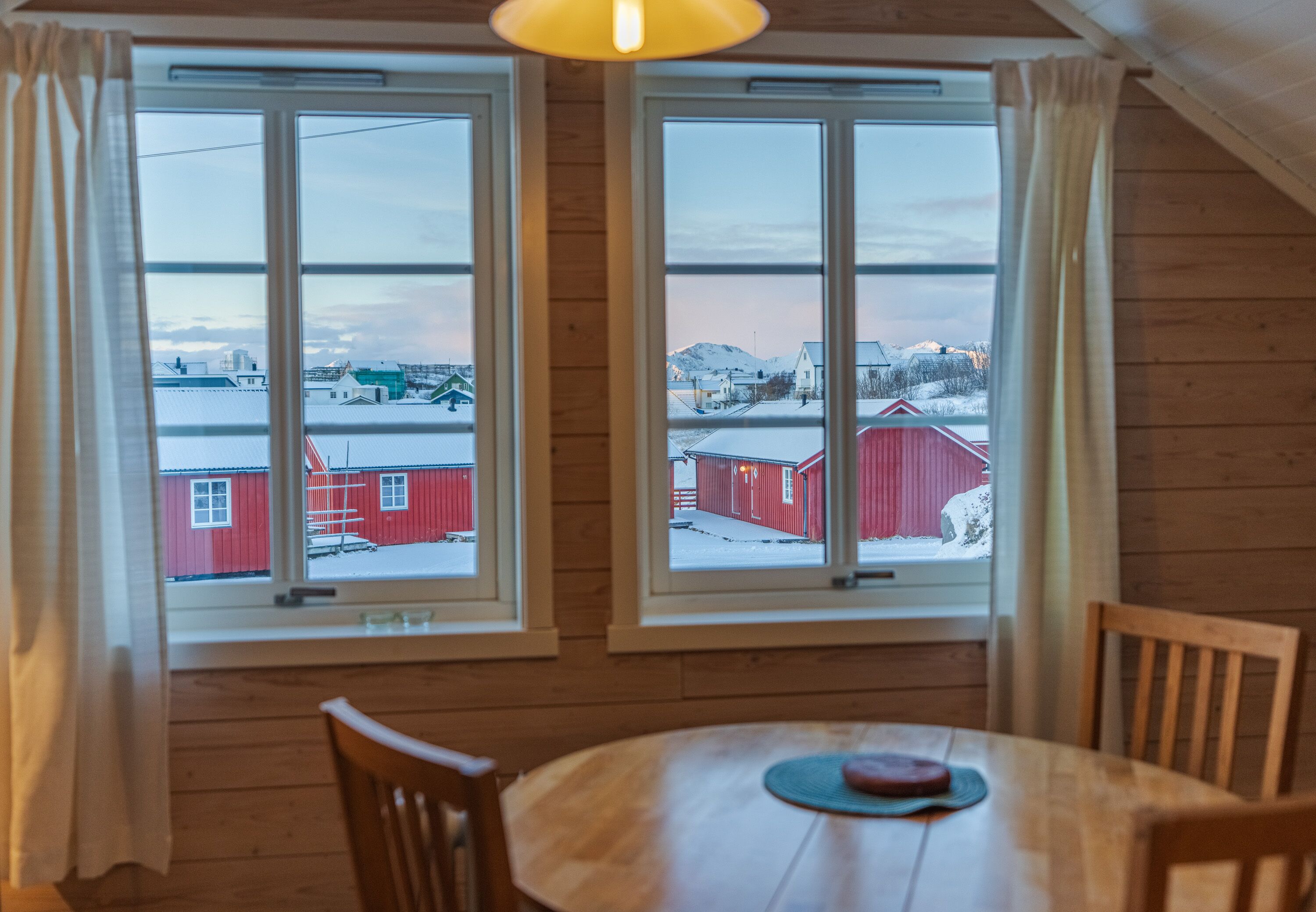 A room with a wooden interior, a round table, and two windows with curtains.