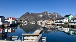 A harbor with boats docked, a wooden pier, and buildings with a mountain backdrop.