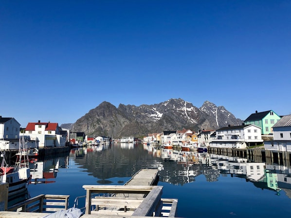 A harbor with boats docked, a wooden pier, and buildings with a mountain backdrop.