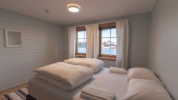 A bedroom with two beds, a window with curtains, a small mirror on the wall, and a view of the water outside.