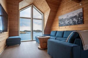 A cozy room with a large window, a blue sofa, a small round table, and a wooden ceiling.